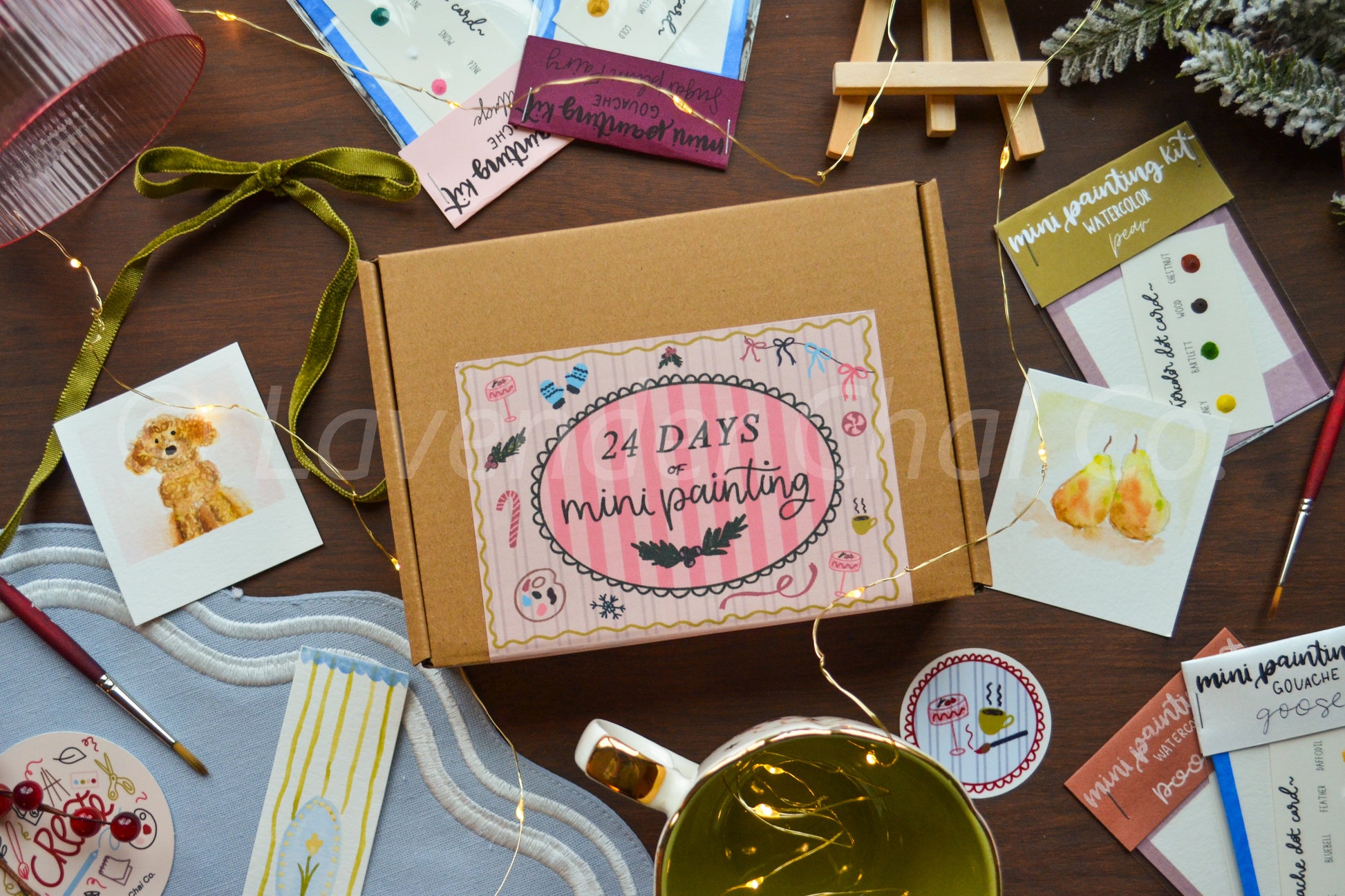 Box labeled '24 Days of Mini Painting' surrounded by small artworks on a wooden surface.