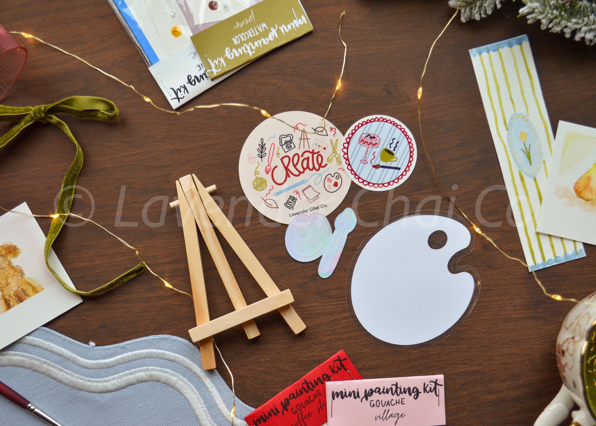 Artistic supplies including a small easel, paint palette, and cards on a wooden surface.