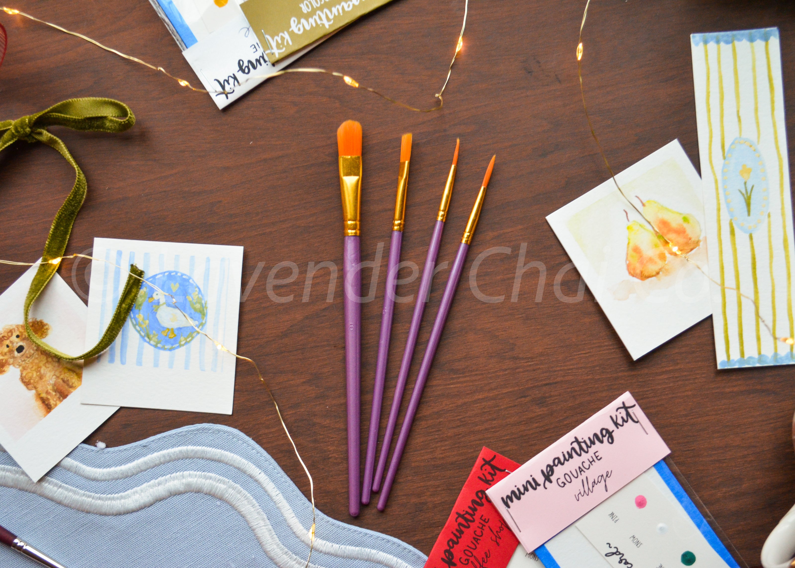 Paintbrushes on a wooden surface with art supplies and cards.